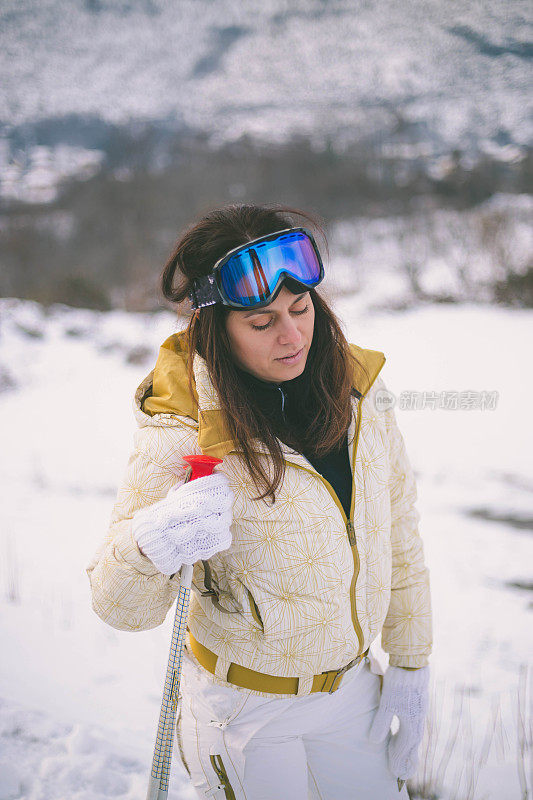 近景美丽的年轻女子在冬天的衣服站在一边，手拿木棍的背景雪山