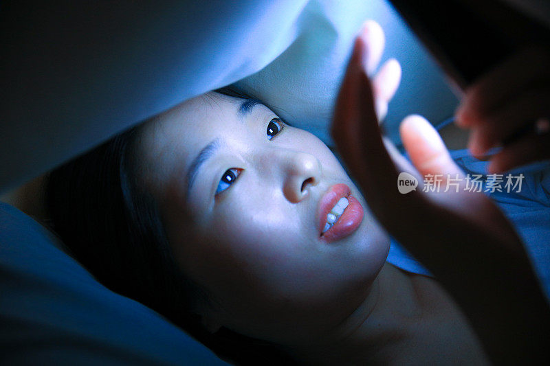 年轻的亚洲女人晚上在床上打电话