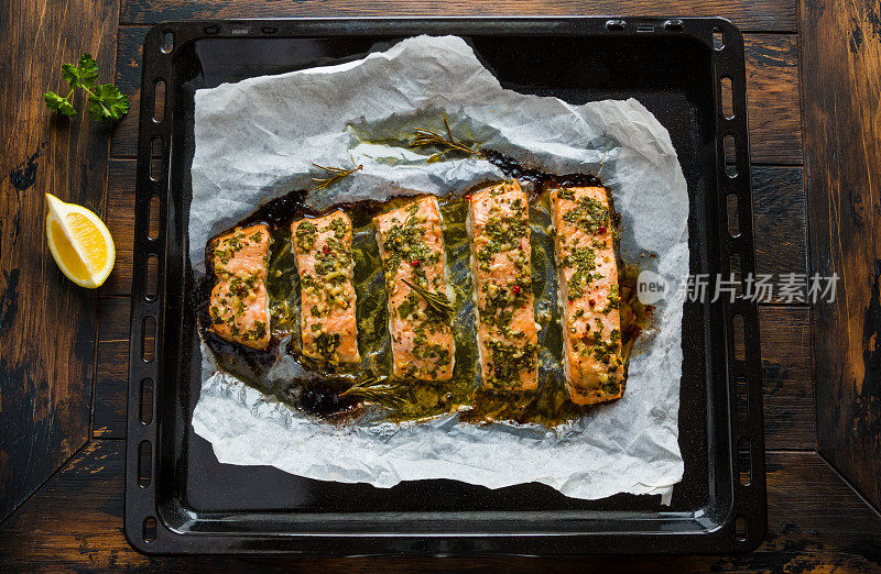 用黄油、欧芹和大蒜在烤箱里烤的三文鱼。烤盘上的熟鱼，木质背景，俯视图。