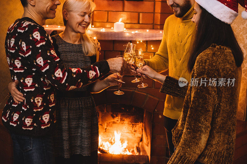 一个成熟的男人、女人和两个年轻人在壁炉边喝着香槟，有说有笑地庆祝圣诞节(或新年)