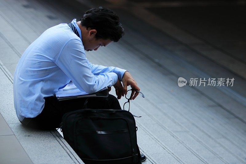 侧面的压力沮丧的年轻亚洲男子坐在楼梯上。他对某事感到失望或疲倦。