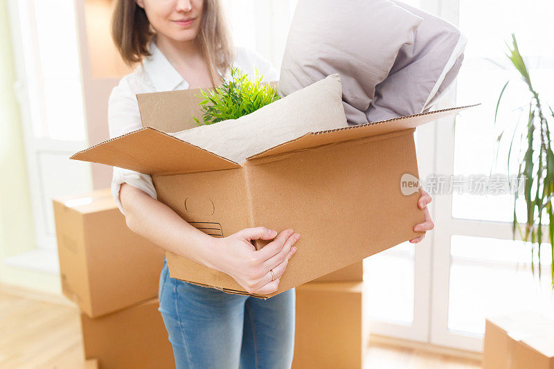 快乐的年轻女子抱着纸箱装着货物和动产，搬到了新家