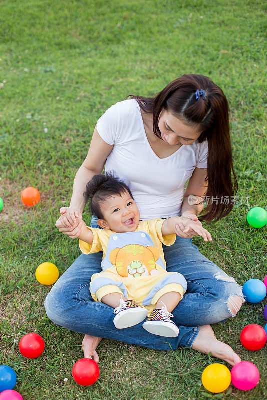 小男孩和妈妈在绿色的草地上玩彩色的球