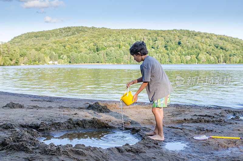 暑假，小男孩在湖边的沙滩上用水填沙洞