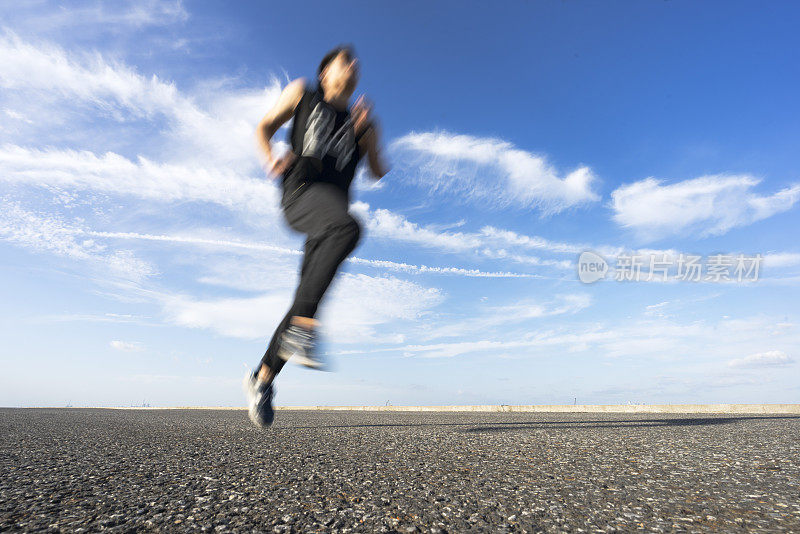 年轻的男运动员在柏油路上迎着天空奔跑