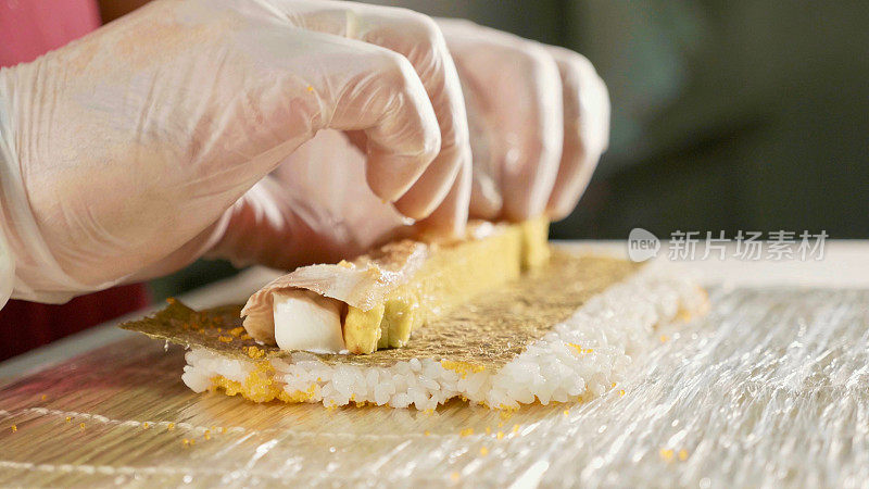 专业寿司厨师在商业厨房准备寿司卷，特写。