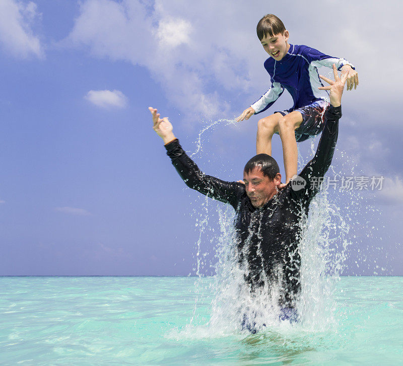 马尔代夫古里希岛海滩上，小男孩在蓝天下从男人的肩膀上跳进水里，享受着碧蓝的海水