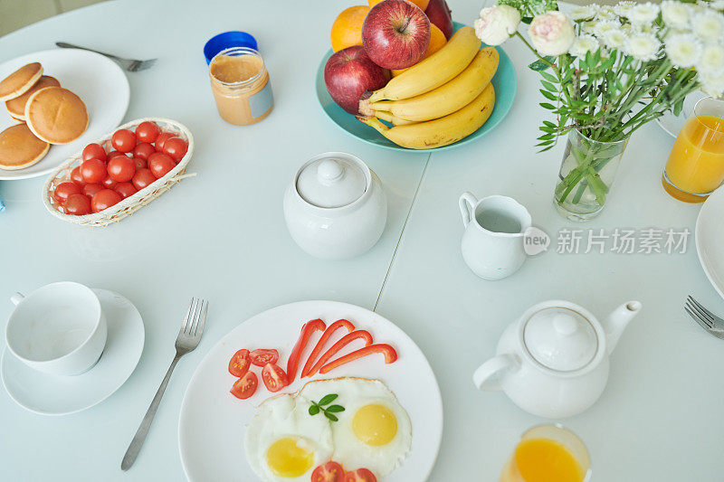 近距离的煎蛋与蔬菜在盘子，茶壶，杯子，鲜花在花瓶，水果和煎饼在桌子上，欧式早餐