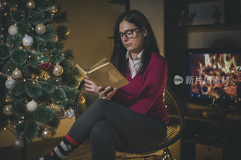 女人坐在圣诞树前的椅子上看书