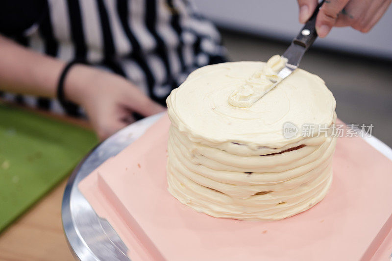 在一个旋转的转盘上用糖霜抹刀给蛋糕上糖霜的女人。蛋糕旋转时运动模糊。