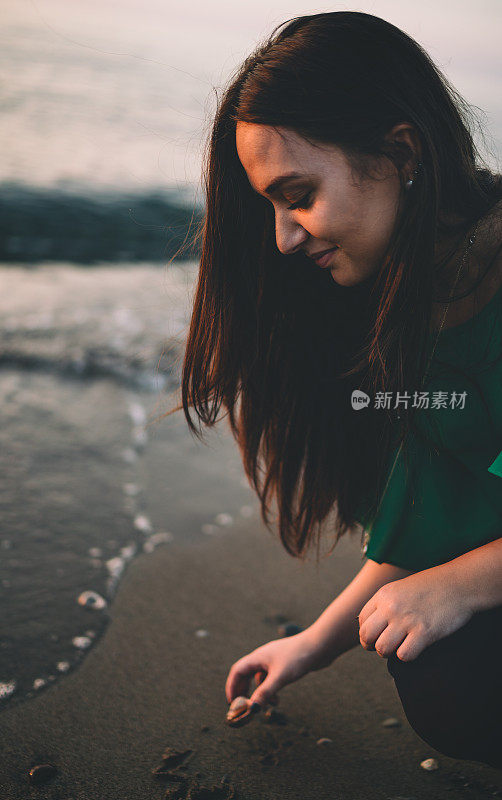 年轻美丽的女人在海滩上收集贝壳