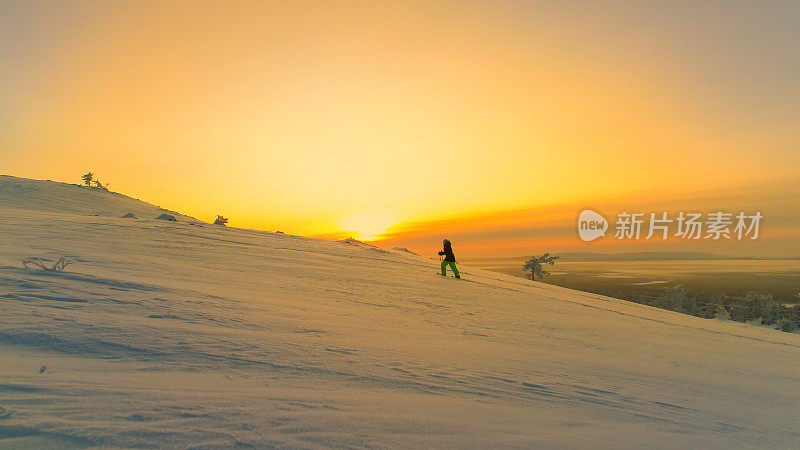 空中镜头:冬天日出时，飞向穿着雪鞋在雪山上徒步旅行的女人