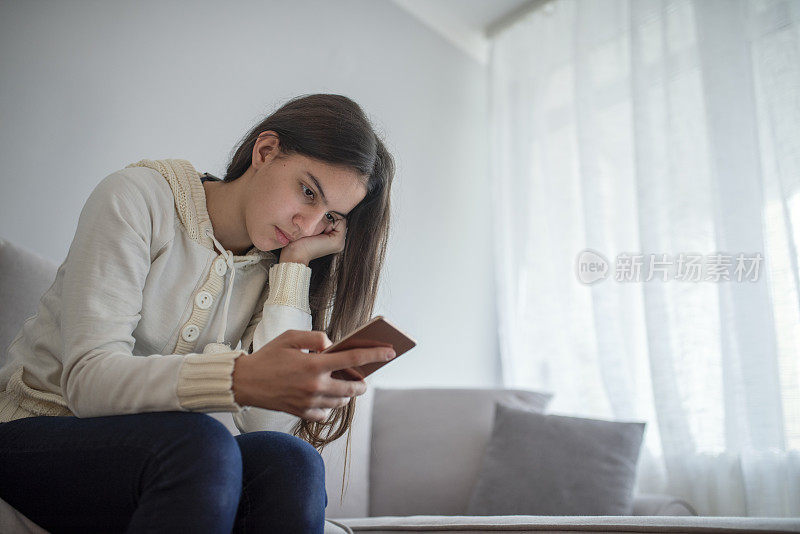 特写的漂亮的十几岁的女孩坐在床上看她的手机