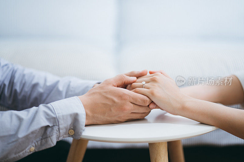 一名男子在新房子里向女友求婚，两人手牵着手，手上还戴着订婚戒指