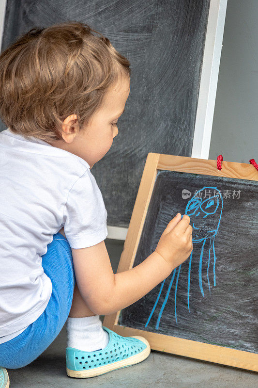 一个三岁的小男孩在黑板上画画