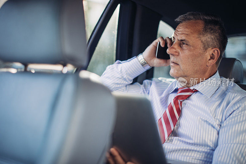 一个商人开车时在汽车后座上使用笔记本电脑
