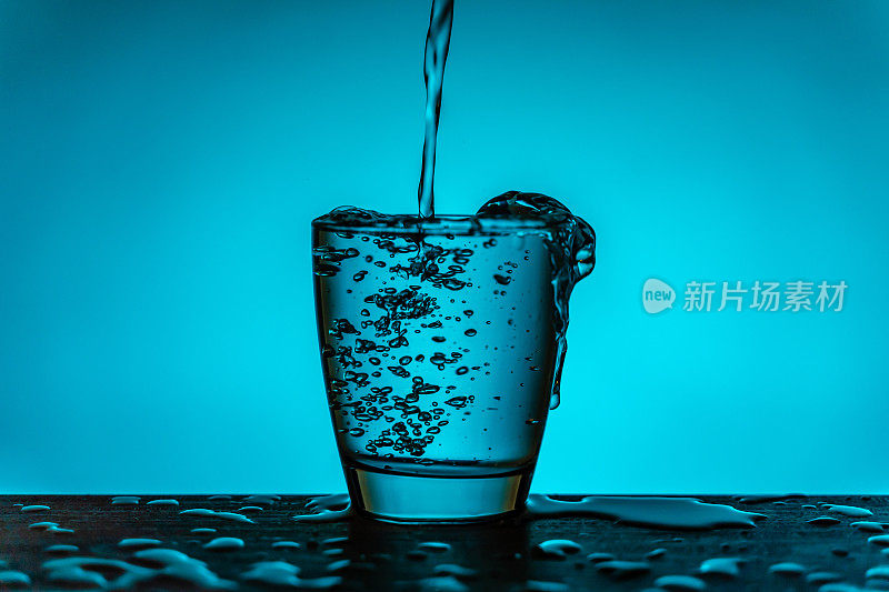 水从水瓶流入玻璃杯-蓝色的背景