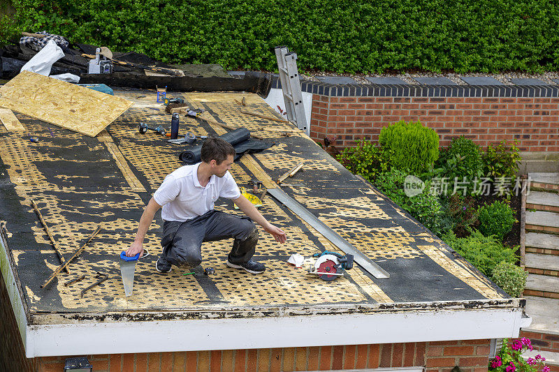 一位木匠正在为车库的平屋顶准备玻璃纤维涂层。