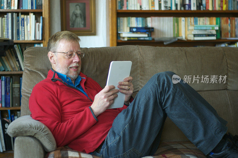 一名留着胡子的中年男子坐在沙发上用平板电脑放松