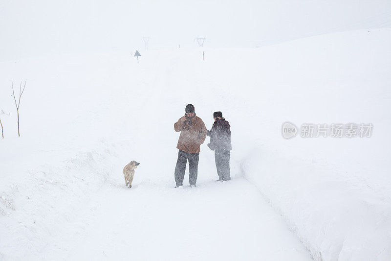 一对老年夫妇在下雪的乡村路上穿着暖和的衣服