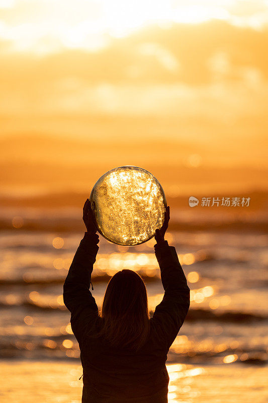 日出时，女人在海滩边拿着水晶球