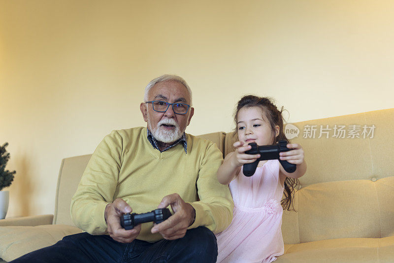英俊的爷爷和可爱的小孙女一起在家玩游戏机。