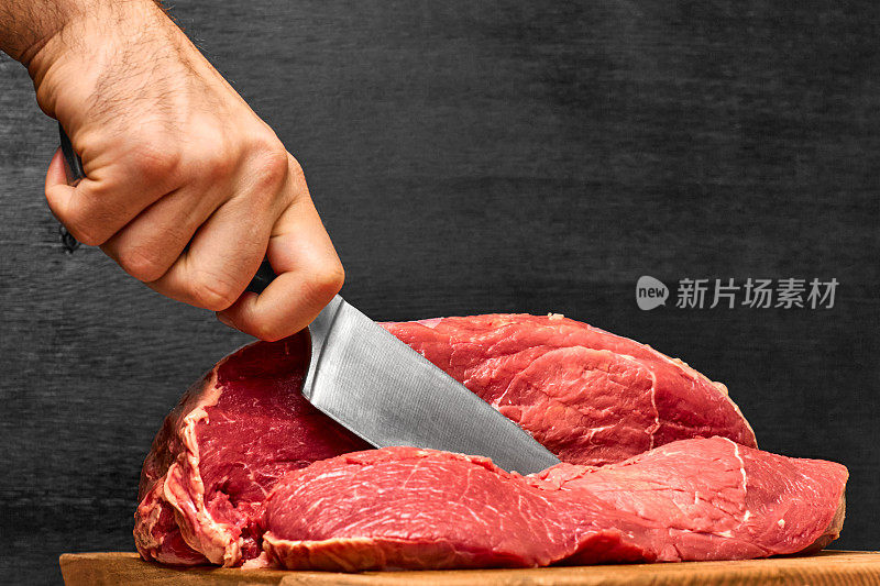 特写男子的手切牛肉与刀在一个黑色的背景。健康蛋白粉的概念。