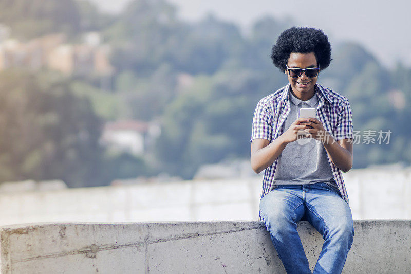 一个年轻的黑人在屋顶上用手机发短信，看起来很开心