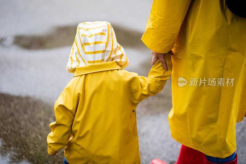 母亲和蹒跚学步的孩子，男孩，在雨中玩耍，穿着靴子和雨衣