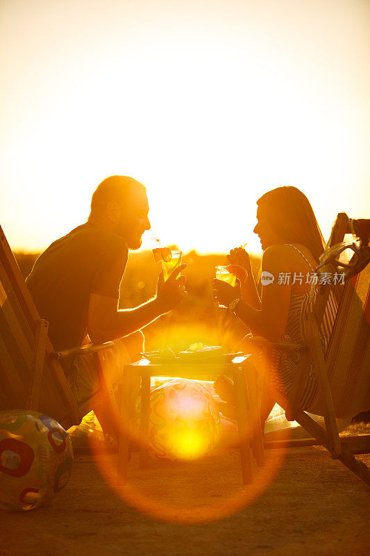 年轻的夫妇在甲板上享受夏日，鸡尾酒和充气