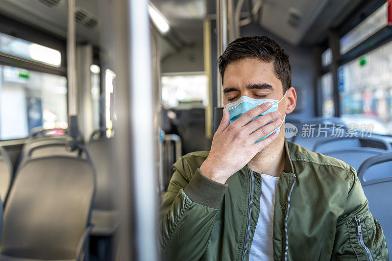 一名戴着医用防护口罩的男子坐在一辆空巴士上。