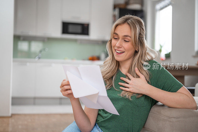 年轻女子微笑着在家里读一封信