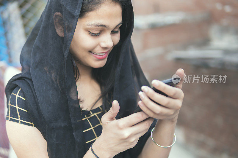 一名印度年轻女子用黑色的dupata盖住她，还在打手机，