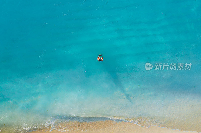 在坦桑尼亚的桑给巴尔岛，一个女人呆在白色的沙滩上，看着海洋中纯净的绿松石般的海水的鸟瞰图