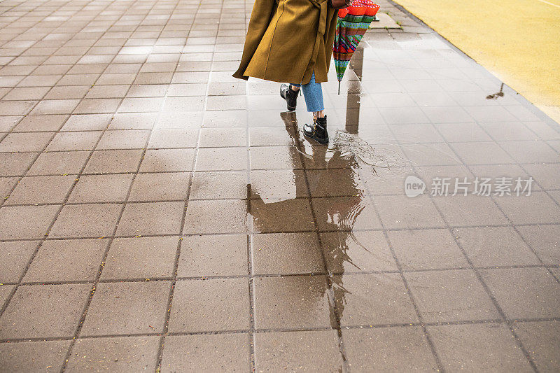 年轻女子撑着伞在雨天走过水坑
