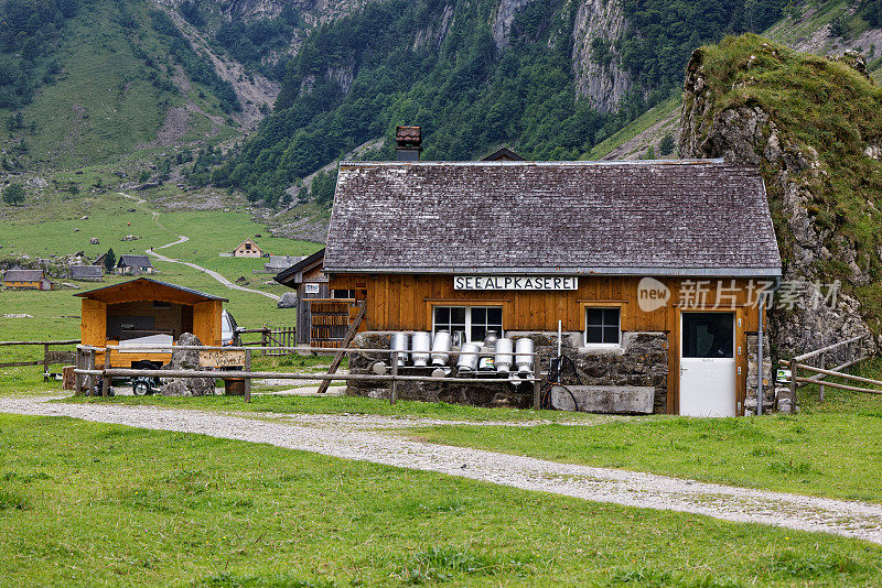 年8月19日瑞士:阿尔卑斯奶酪农场，建在石墙旁边，房子前面的空牛奶罐，德国阿尔卑斯奶酪农场标识，文本翻译:阿尔卑斯奶酪农场