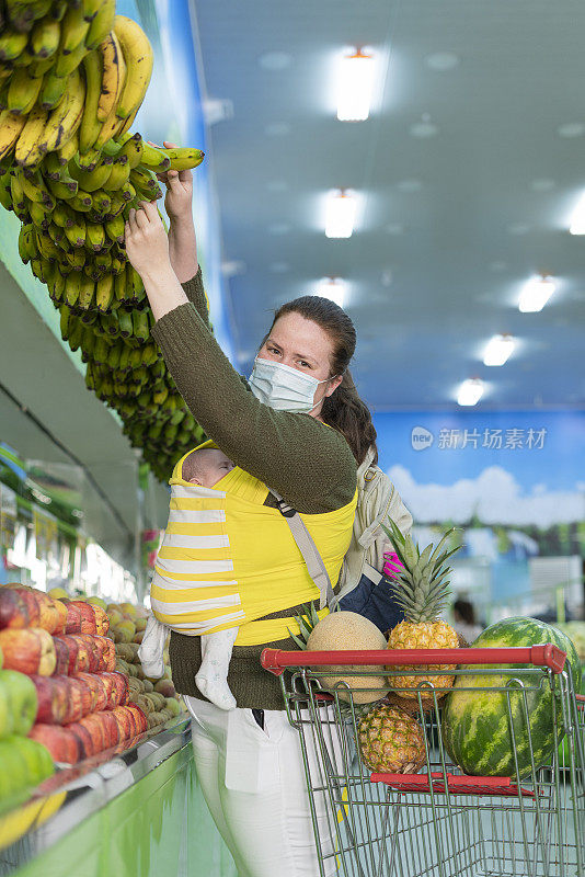 年轻的妇女抱着她的孩子在超市的水果和蔬菜选择他们的食物时看着相机的肖像