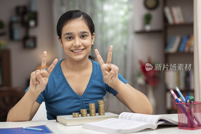 一个十几岁的女学生在家里学习和做一堆硬币:库存照片