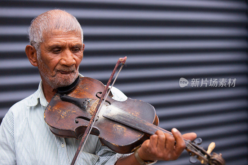 一个满脸皱纹，头发稀疏灰白的老音乐家，在街上用小提琴弓拉着小提琴，他热爱他的职业。