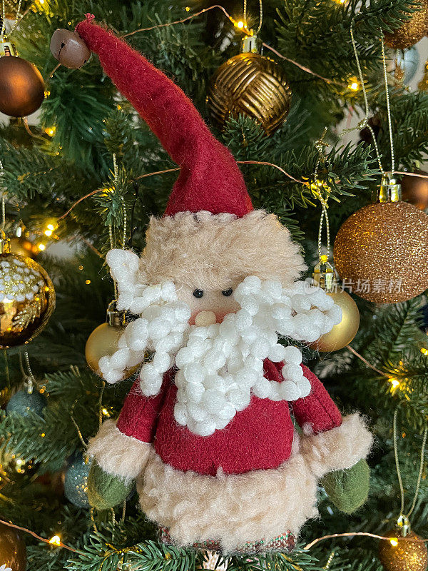 近距离图像的圣诞老人与羊毛圈胡子装饰周围的金和铜彩色的小饰品挂在人造圣诞树的树枝上，雪花，云杉针，模糊的白色神仙灯的背景