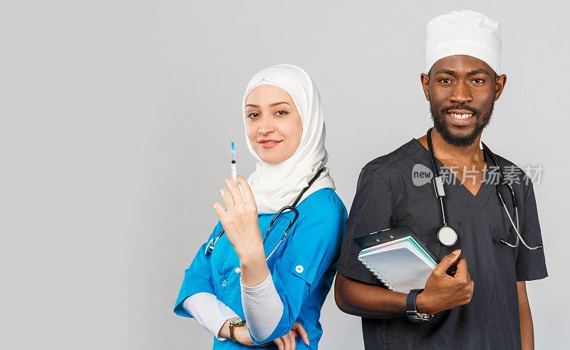 在浅灰色的背景下，医疗小组站在一起。非裔美国外科医生和医生穆斯林妇女听诊器