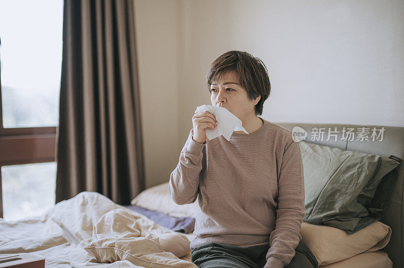 亚洲华人中年妇女用纸巾咳嗽，感觉不舒服，生病在家卧室休息