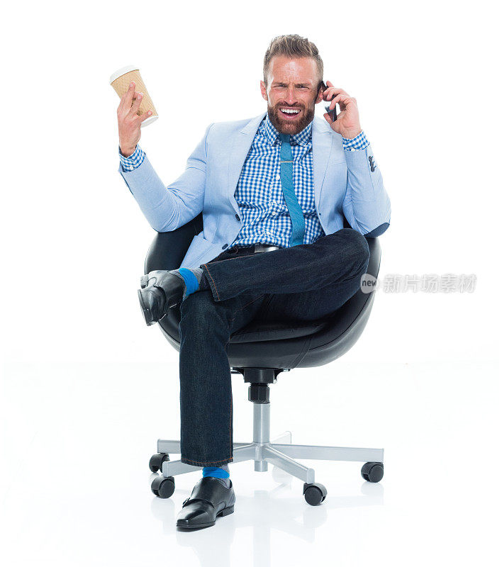 白人年轻男性商人，打着领带坐在白色背景前面，拿着咖啡杯，用手机