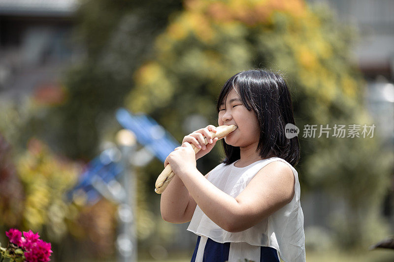 亚洲中国可爱的小女孩喜欢在阳光明媚的日子里在公园里吃她最喜欢的面包