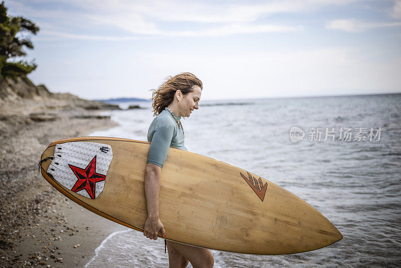 拿着冲浪板的女人站在水边看浪。