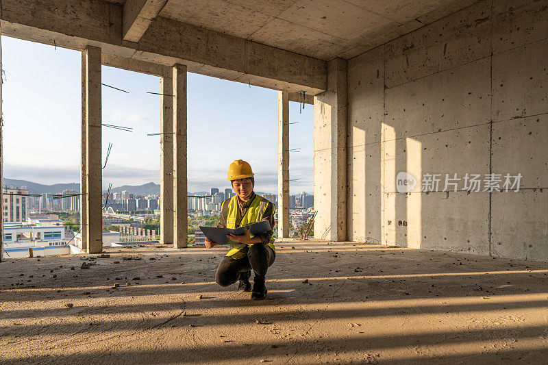 阳光透过建筑工地，一名女工程师蹲在地上拿着文件夹查看数据