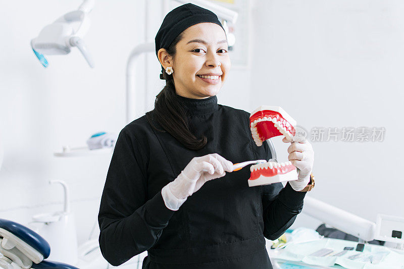 微笑的女牙医展示假牙，牙医解释刷牙，女牙医展示假牙和牙刷