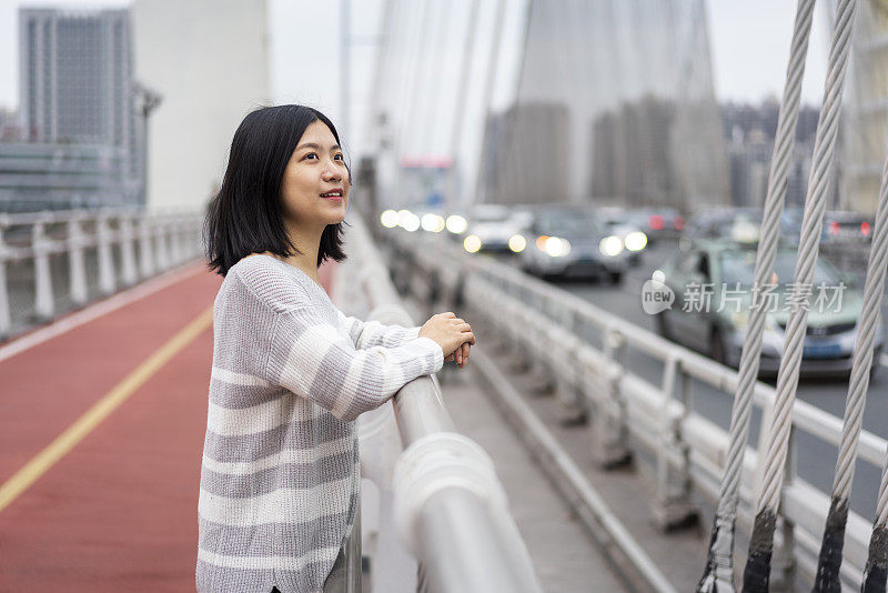 在市中心的一座桥上，一位亚洲妇女望着远方