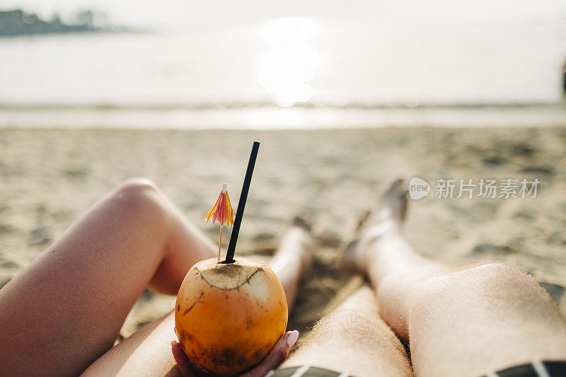 一对年轻夫妇在海滩上喝着椰子鸡尾酒