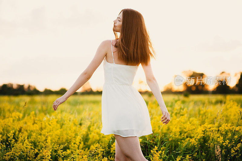 可爱的年轻女子，一头乌黑的长发，穿着白色的衣服，在阳光明媚的日子里微笑着在草地上奔跑